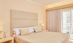 Rom med en dobbeltseng, beige sengetøy og lampe på nattbordet ved siden av vindu med gardiner. (AI-generert tekst)