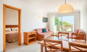 En hotellsuit med et bord, stoler, sofa og et soverom synlig gjennom en åpen dør. (AI-generert tekst)