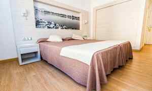 Hotellrom med en stor seng dekket med et brunaktig sengeteppe og hvitt sengetøy, med tregulv og en veggdekorasjon i form av et svart-hvitt bilde. (AI-generert tekst)