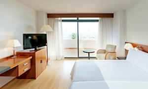 Et hotellrom med to senger, en TV på en trekommode og en glassdør som fører ut til en terrasse. (AI-generert tekst)