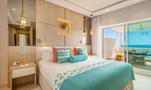 Hotellrom med dobbeltseng, dekorert i blått og hvitt, med utsikt over havet fra en balkong. (AI-generert tekst)