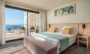 Hotellrom med seng, sittemøbler og utsikt mot havet gjennom store vinduer. (AI-generert tekst)