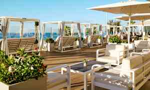 Loungeområde med sittegrupper og solsenger under parasoller, samt havutsikt. (AI-generert tekst)