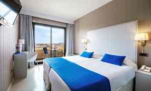 Et hotellrom med en dobbeltseng, lyse vegger og blått sengetøy. (AI-generert tekst)