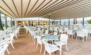 En utendørs restaurant med mange hvite bord og stoler under et tak. (AI-generert tekst)