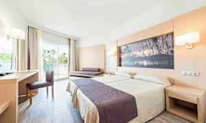 Et hotellrom med en dobbeltseng, skrivebord, stol og en sofa. Rommet har en glassdør som fører til en balkong. (AI-generert tekst)