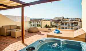 Terrasse med boblebad, sofa og utsikt over omkringliggende bygninger. (AI-generert tekst)