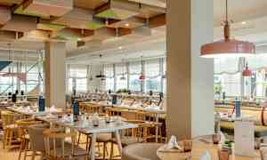 Restaurant med lyse møbler og dekorert tak. (AI-generert tekst)