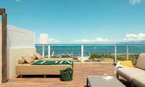 Terrasse med moderne møblering og utsikt over havet, inklusive en solseng, sofamøbler og bord. (AI-generert tekst)