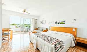 Et hotellrom med lys innredning, to enkeltsenger, en sofa, et bord og stoler samt en balkong med utsikt. (AI-generert tekst)