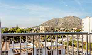 Utsikt fra en balkong over bygninger med tegltak og omkringliggende bylandskap, med et fjell i bakgrunnen. (AI-generert tekst)