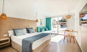 Hotellrom med en dobbeltseng, en sofa med puter, et lite spiseområde og en balkong. (AI-generert tekst)