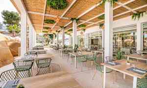 Utendørsrestaurant med bord og stoler under et tak med grønne planter. (AI-generert tekst)