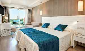 Hotellrom med to senger, en sofa og en glassbalkong. (AI-generert tekst)