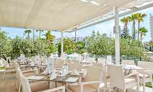 Restaurant med hvite møbler og tak, omgitt av grøntområder. (AI-generert tekst)