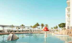 Bilde av et basseng med en sklie formet som et sneglehus og en soppformet vannfontene. Solsenger og parasoller er synlige i bakgrunnen. (AI-generert tekst)