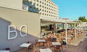 Hotellfasade og utendørsservering med bord og stoler, mennesker som sitter og spiser. (AI-generert tekst)