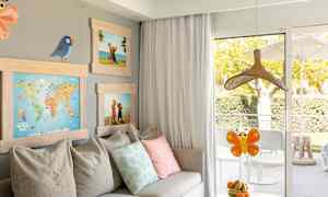 Et rom med en sofa, puter, bilder samt et bord med en bolle med frukt foran en balkongdør. (AI-generert tekst)