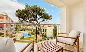 Utsikt fra en balkong med sittemøbler, mot en indre gårdsplass med basseng og omkringliggende bygninger. (AI-generert tekst)