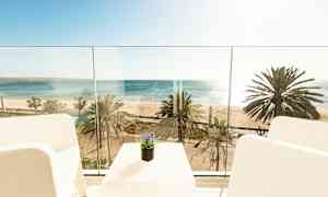 Utsikt fra en balkong mot havet og stranden med palmer. (AI-generert tekst)