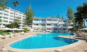 Et utendørs svømmebasseng med solsenger og parasoller foran en hvit bygning, omgitt av trær. (AI-generert tekst)