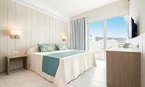 Et lyst hotellrom med en dobbeltseng kledd i hvit og turkis sengetøy, to nattbord, en garderobe og en balkong med utsikt over byen. (AI-generert tekst)