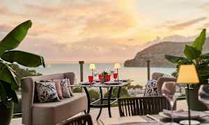 Utendørs servering med bord og sofaer, omgitt av grønn vegetasjon, med utsikt over havet under en solnedgang. (AI-generert tekst)