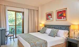 Et hotellrom med en dobbeltseng, nattbord, to bordlamper og en stol ved et skrivebord. Bak sengen henger to bilder på veggen. (AI-generert tekst)