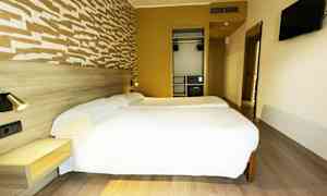 Et hotellrom med to enkeltsenger, en veggmontert TV og en garderobe. (AI-generert tekst)