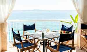 Utsikt over et oppdekket bord med blå stoler og hav i bakgrunnen. (AI-generert tekst)