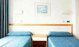 To enkeltsenger med blå sengetepper og en trepanel bak. (AI-generert tekst)