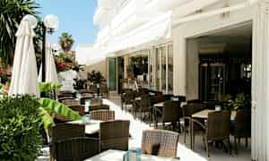 Utendørs servering med mørke rottingstoler og hvite bord, omgitt av grøntområder. (AI-generert tekst)