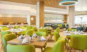 Interiør av en restaurant med grønne stoler og dekkede bord. (AI-generert tekst)