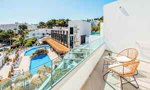 Utsikt fra en balkong med to stoler og et bord mot et basseng og bygninger omgitt av grøntområder. (AI-generert tekst)