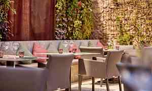 En uteplass med sitteplasser og dekorerte vegger, omgitt av grøntområder. (AI-generert tekst)