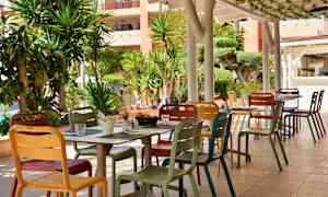 En utendørsterrasse med fargerike stoler og bord, omgitt av frodige planter. (AI-generert tekst)