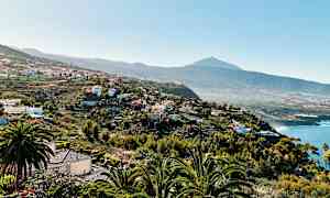 En utsikt over et kupert landskap med hus og vegetasjon samt en fjelltopp i bakgrunnen. (AI-generert tekst)