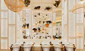 Interiør av en restaurant med bord, stoler og planter i en lys og moderne design. (AI-generert tekst)