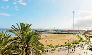 En strand med palmer, mennesker og bygninger i bakgrunnen. (AI-generert tekst)