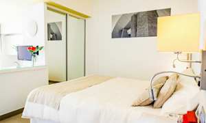 Et moderne og lyst hotellrom med hvitt interiør, en dobbeltseng og et innebygd speilgarderobeskap. (AI-generert tekst)
