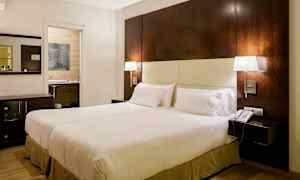 Et hotellrom med en stor seng, to sengelamper, et nattbord og en telefon. En åpning mot et bad ligger i bakgrunnen. (AI-generert tekst)