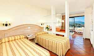 Et hotellrom med to enkeltsenger, en sittegruppe og balkong. (AI-generert tekst)