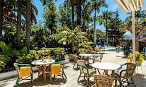 Utendørs serveringsområde med bord og stoler nær et basseng og frodig vegetasjon. (AI-generert tekst)