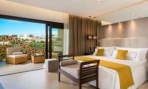 Et moderne hotellrom med en stor seng og sittemøbler, samt en åpning mot en balkong med utsikt. (AI-generert tekst)