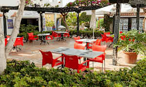 Utendørs servering med røde stoler og bord, omgitt av vegetasjon. (AI-generert tekst)