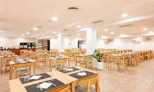 En spisesal med trebord og stoler. Rommet er lyst og romslig med duker og oppsatte glass. (AI-generert tekst)