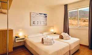 Et lyst hotellrom med en dobbeltseng, vindu med utsikt over landskapet og et veggmaleri over sengen. (AI-generert tekst)