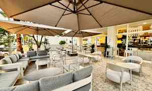Utendørs serveringsområde med sofaer og bord under parasoller. (AI-generert tekst)