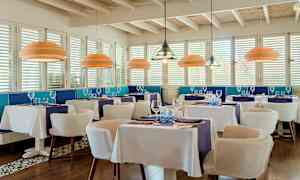 En elegant restaurant med hvite duker, blå dekor og moderne taklamper. (AI-generert tekst)