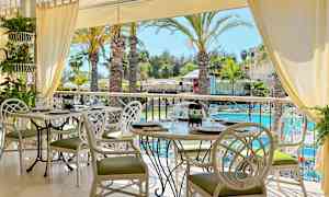 En restaurant med hvite bord og stoler, utsikt over palmer ved et basseng. (AI-generert tekst)